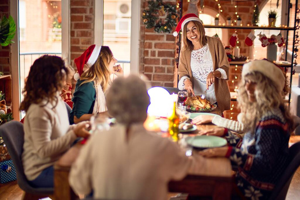 Beautiful group of women smiling happy and confident. Carving roasted turkey celebrating christmas at home - 写真・画像