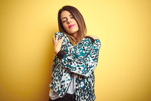 Young beautiful woman wearing casual jacket over yellow isolated background Hugging oneself happy and positive, smiling confident. Self love and self care - 写真・画像