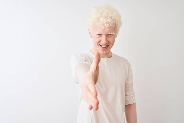 Young albino blond man wearing casual t-shirt standing over isolated white background smiling friendly offering handshake as greeting and welcoming. Successful business. - Foto, immagini