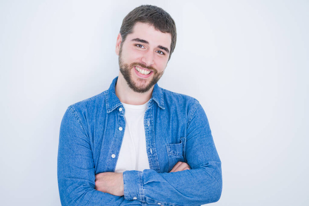 junger gutaussehender hispanischer Mann, der mit verschränkten Armen in die Kamera lächelt und glücklich und zuversichtlich über den isolierten weißen Hintergrund blickt - Foto, Bild