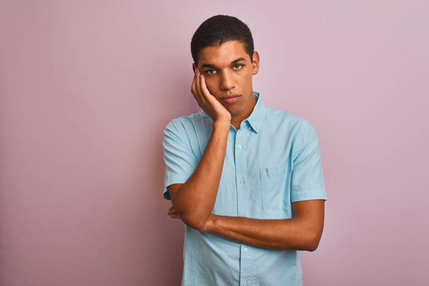 Молодий красивий арабський чоловік у синій сорочці стоїть над ізольованим рожевим фоном думаючи, що виглядає втомленим і нудним від проблем депресії з схрещеними руками
. - Фото, зображення