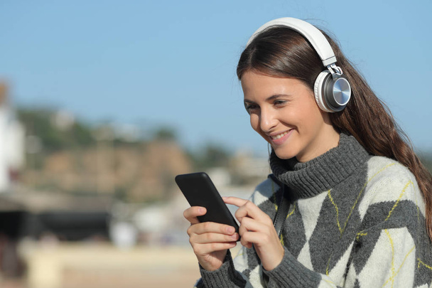 Happy girl słuchanie muzyki przy użyciu telefonu komórkowego w zimie - Zdjęcie, obraz