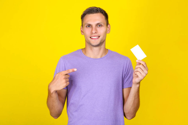 Young man with blank business card on yellow background - Zdjęcie, obraz