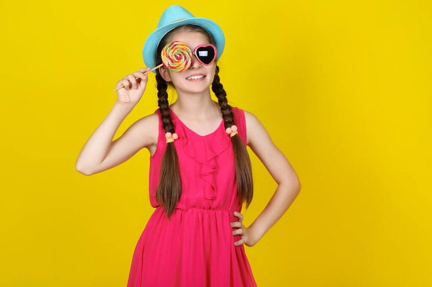 Beautiful young girl with sweet lollipop on yellow background - Fotó, kép