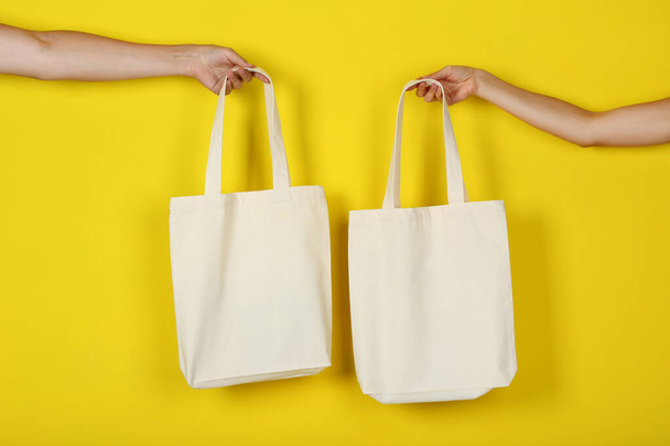 Female hands holding white cotton eco bags on yellow background - Foto, afbeelding
