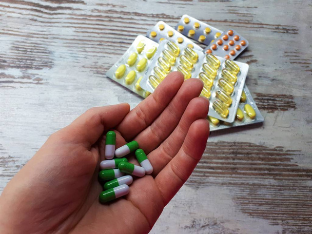close-up van de handpalm met geneesmiddelen van groen-witte kleur tegen de achtergrond van verschillende geneesmiddelen van geel-oranje kleur in blaren - Foto, afbeelding