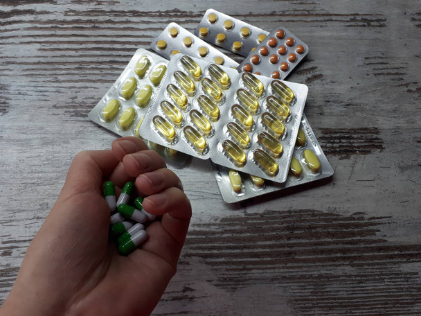  közeli kép a tenyér a gyógyszerek zöld-fehér színű háttér különböző gyógyszerek sárga-narancs színű buborékcsomagolásban - Fotó, kép