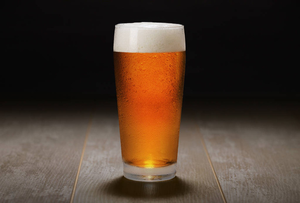 Double India pale ale beer served in a chilled pint glass on wooden counter at a craft beer pub, black background - 写真・画像