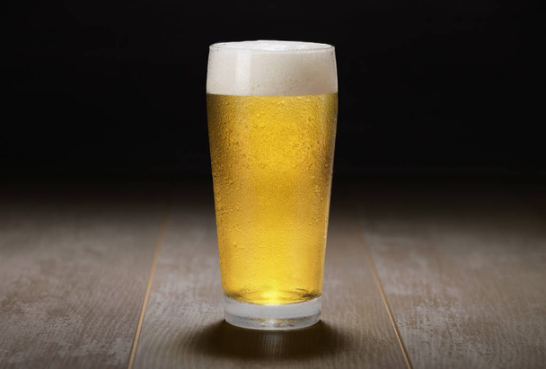 Egy pohár világos sör, világos sör, sörcsapolás fa felületen és fekete háttér - Fotó, kép