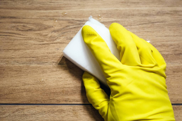Una mano in un guanto di gomma giallo pulisce piastrelle bagnate imitando una superficie di legno con una spugna di melamina bianca. Pulizia in un bagno moderno. Focus selettivo
 - Foto, immagini