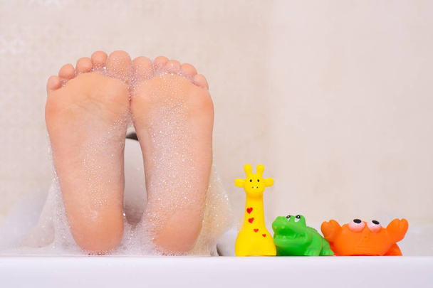 Cute little baby girl biorąc kąpiel bawiąc się pianką i kolorowe gumowe zabawki w białej łazience.  - Zdjęcie, obraz