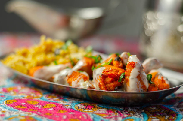 Cijfers van gekookte gemarineerde kipfilet in een ui en tomatensaus met yoghurt en munt en knapperige gebakken uien gelaagd met gekruide basmatirijst, Indiaas eten - Foto, afbeelding
