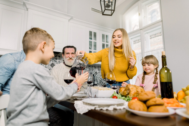 Досить молода мати виливає вишневий сік для сина на святкову вечерю. щаслива велика сім'я проводить святкову вечерю в день подяки
 - Фото, зображення