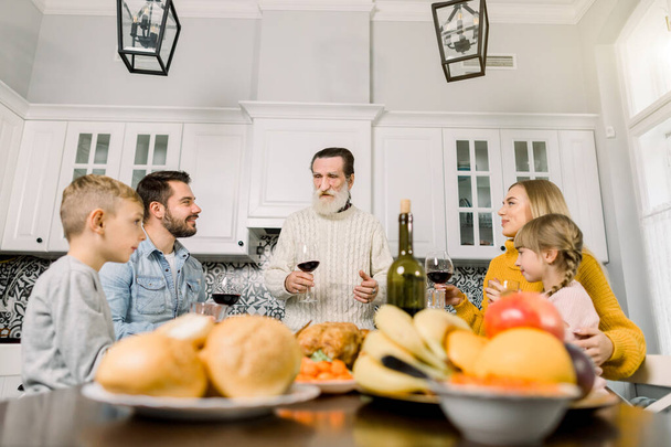 Familia Multi Generación Celebrando Acción de Gracias. Viejo abuelo con barba gris sostiene vaso con vino tinto y habla de los deseos y tostadas
 - Foto, Imagen