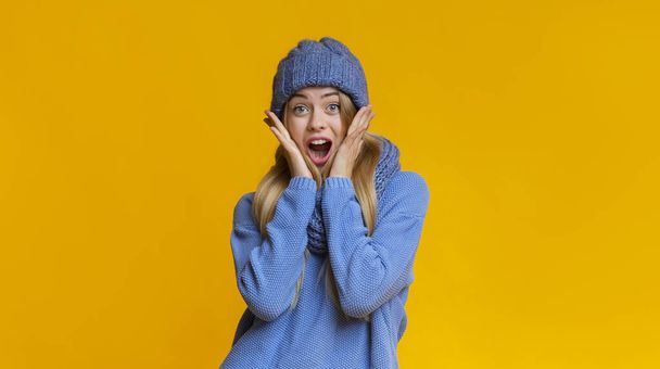 Amazed girl in winter hat touching her cheeks with palms - Фото, изображение