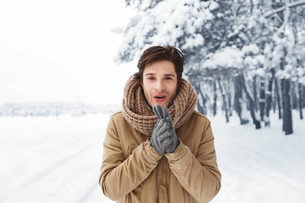 Счастливчик в перчатках растирает руки, стоя в зимнем лесу
 - Фото, изображение
