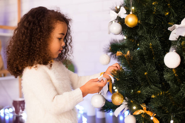 Little afro girl decorating Xmas tree at home, free space - Photo, Image
