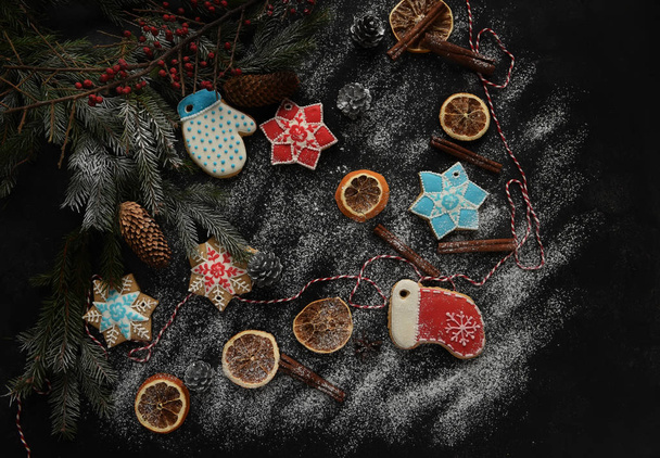 Biscuits au pain d'épice et biscuits de Noël parmi les branches d'un arbre de Noël dans la neige artificielle sur un fond noir. Décorations de Noël, carte postale. Préparation de la nouvelle année et de l'alcool de Noël
 - Photo, image