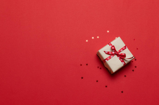 ギフトボックスまたはプレゼントボックス付きのお祝いカード、赤いテーブルの上のコンフェッティ。誕生日、母の日、陽気なクリスマスと新年のためのフラットレイアウト組成 - 写真・画像