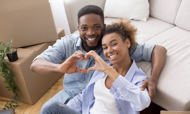 Afro Spouses Gesturing Heart Shape Hugging Among Moving Boxes Indoor - Fotografie, Obrázek