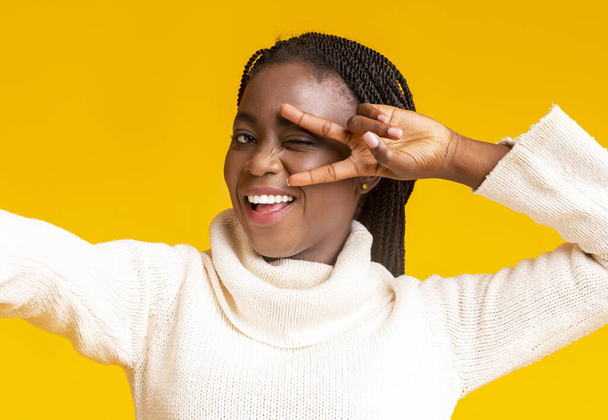 Carefree black girl taking selfie, covering eye with fingers - Photo, Image