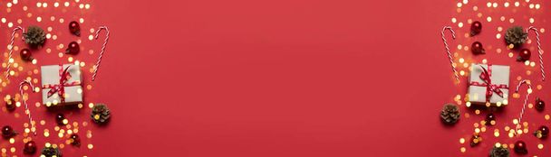 Composizione natalizia con scatola regalo di carta rossa, nastro, caramelle e palline di Natale di diverse dimensioni su sfondo rosso con spazio per la copia. Design idea creativa laica piatta
 - Foto, immagini