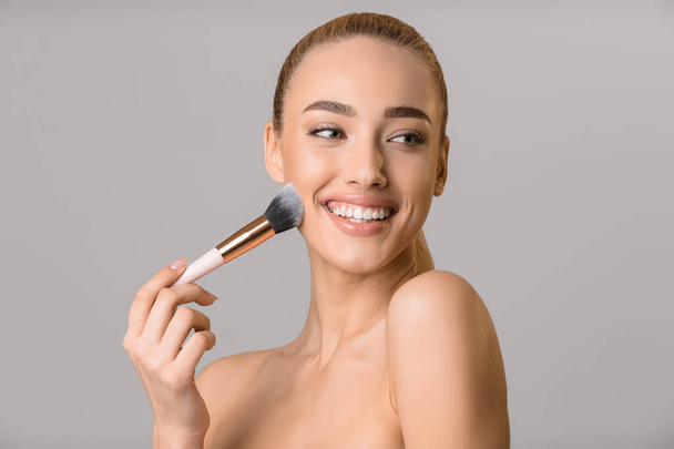Mujer joven usando cepillo, aplicando maquillaje, fondo gris
 - Foto, Imagen