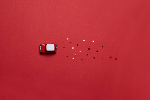 Flat lay of Christmas composition of cards with a red model of a children car toy with glitter candy on a red saturated background. Holiday delivery idea concept - Photo, Image
