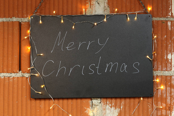 Merry Christmas - The inscription on the black chalkboard is illuminated by garlands - Fotoğraf, Görsel