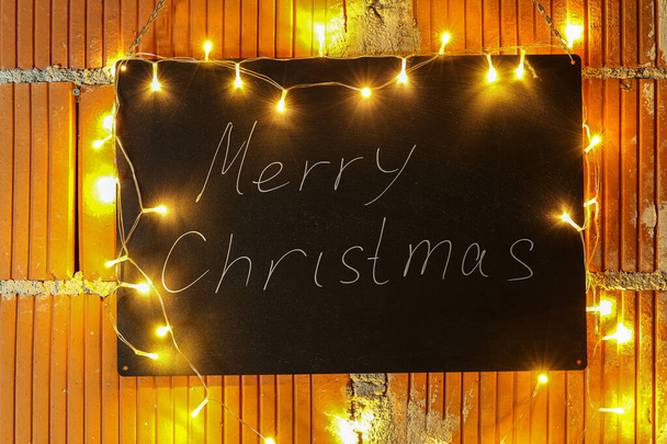 Merry Christmas - The inscription on the black chalkboard is illuminated by garlands - Fotó, kép