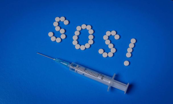 Spuit en Sos van pillen op een blauwe achtergrond. Verslavingsconcept en hiv-preventie - Foto, afbeelding