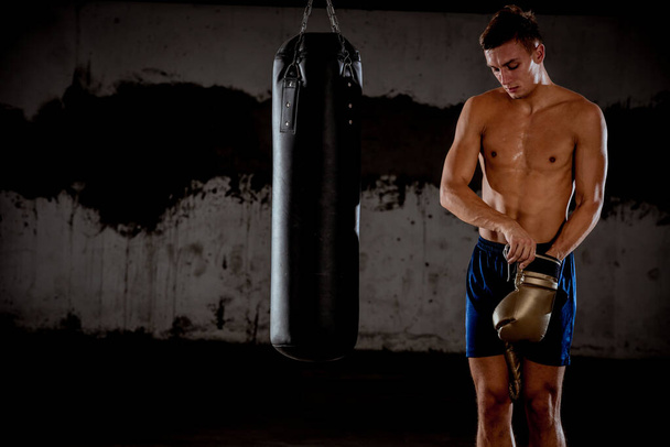Combattant musculaire pratiquant quelques coups de poing avec sac de boxe dans des gants de boxe. Le concept d'un mode de vie sain
 - Photo, image