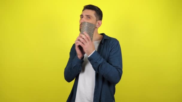 A young man in a white T-shirt with a gift in his hands, cowards a box near his ear and tries to understand what's inside, yellow background. Holidays concept: New Year, Christmas, birthday. 4kfootage - Filmmaterial, Video