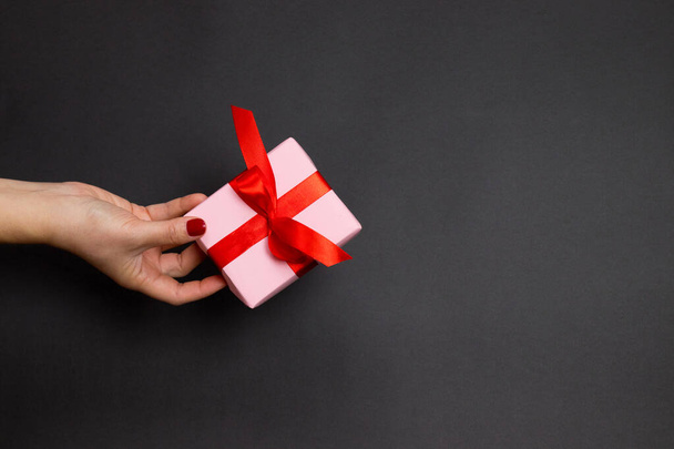 女性の手で幸せな休日のコンセプトは暗い背景に赤いアトラスリボンと驚きの贈り物を保持しています。フラットレイアウト、トップビュー - 写真・画像