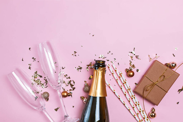 Creative composition with bottle of a champagne, two champagne glasses, gold baubles and confetti on pink background - Photo, image