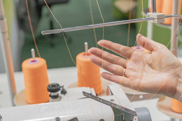 Sewing machine operator sets up a machine. Orange sewing spools are on the background. - Φωτογραφία, εικόνα