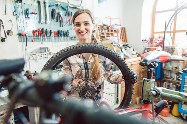 Bisiklet tamircisi kadın bisiklet tekerleğinden bakıyor - Fotoğraf, Görsel