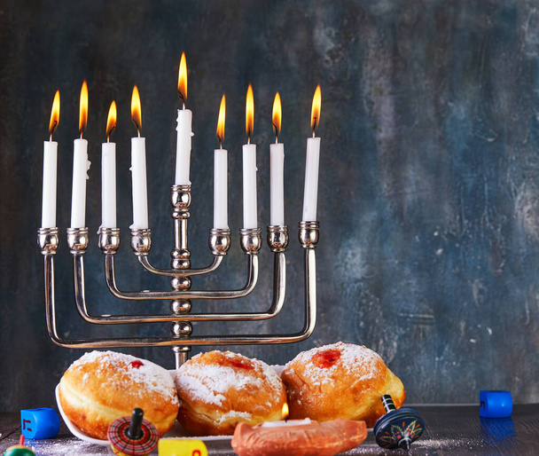 Vacanza ebrea sfondo Hanukkah. Un piatto tradizionale sono le ciambelle dolci. Hanukkah tavolo impostazione di un candelabro con candele e trottole su uno sfondo blu. Copia spazio
 - Foto, immagini