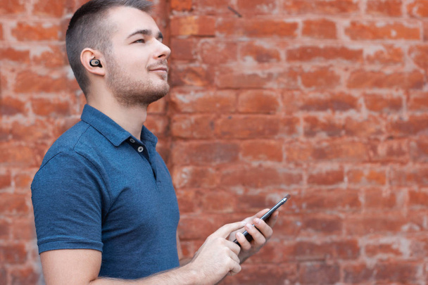 Hombre moderno escuchando música por auriculares bluetooth. Guy controla los auriculares inalámbricos desde su teléfono inteligente. Mantenerse al día con la persona de tecnología. Espacio vacío
 - Foto, Imagen