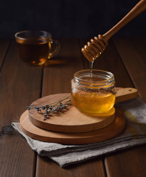 Natural floral honey drains to jar on wood background. Front view - 写真・画像