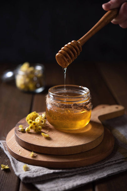 Natural floral honey drains to jar on wood background. Front view - Photo, Image