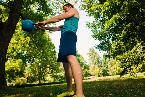 Muskelprotz trainiert mit Kettlebell auf Gras im Park - Foto, Bild