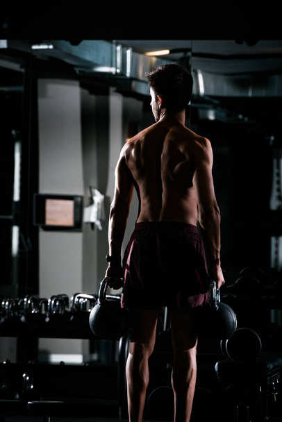 Hoikka lihaksikas mies nostaa painoja kuntosalilla
 - Valokuva, kuva