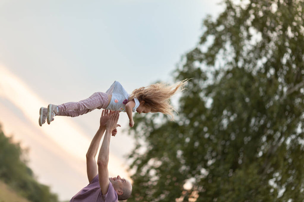 Father throws a happy daughter high in the sky, sunset, summer - Fotografie, Obrázek