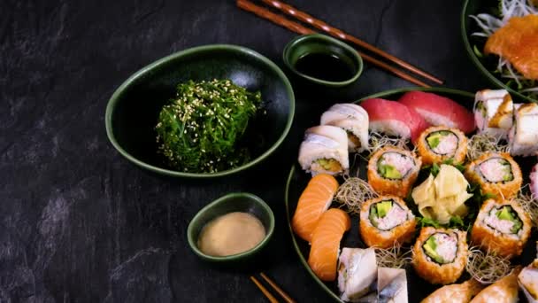 Siyah arkaplan üzerine kurulmuş çeşitli suşilerin slaytlarını kapat. Geleneksel Japon yemekleri. Havyarlı suşi rulosu, somon, yılan balığı ve karides sashimi, uskumru, ton balığı nigiri, wakame salatası. 4k - Video, Çekim