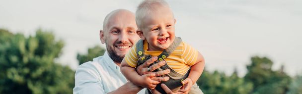Beyaz bir baba, yeni yürümeye başlamış bir bebekle oynuyor. Çocuğunu kucağında taşıyan bir ebeveyn. Otantik yaşam tarzı aile hayatı anı. Mutlu babalar. Web sayfası başlığı. - Fotoğraf, Görsel