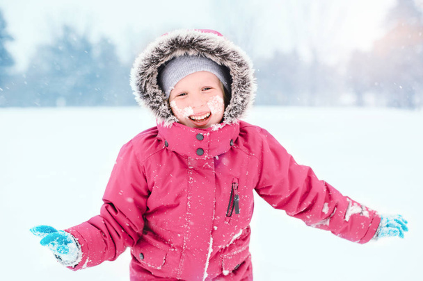 Portrait of cute Caucasian smiling laughing excited girl child in pink jacket playing with snow during cold winter snowy day at snowfall. Kids outdoor seasonal activity. Funny face. - Photo, Image