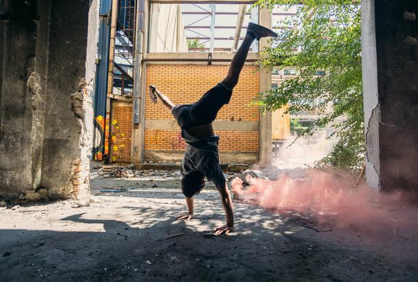 Young man doing parkour handstand around colored smoke bomb - 写真・画像