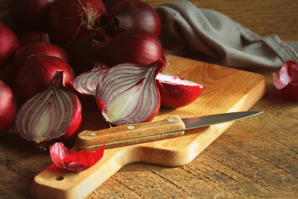 Red onions on wooden chopping cutting board over dark wooden rustic texture background. Top view, space for text - Zdjęcie, obraz