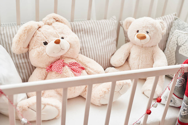 Rabbit and bear in white crib.Soft toys in children's bedroom. White kids room. - Photo, Image